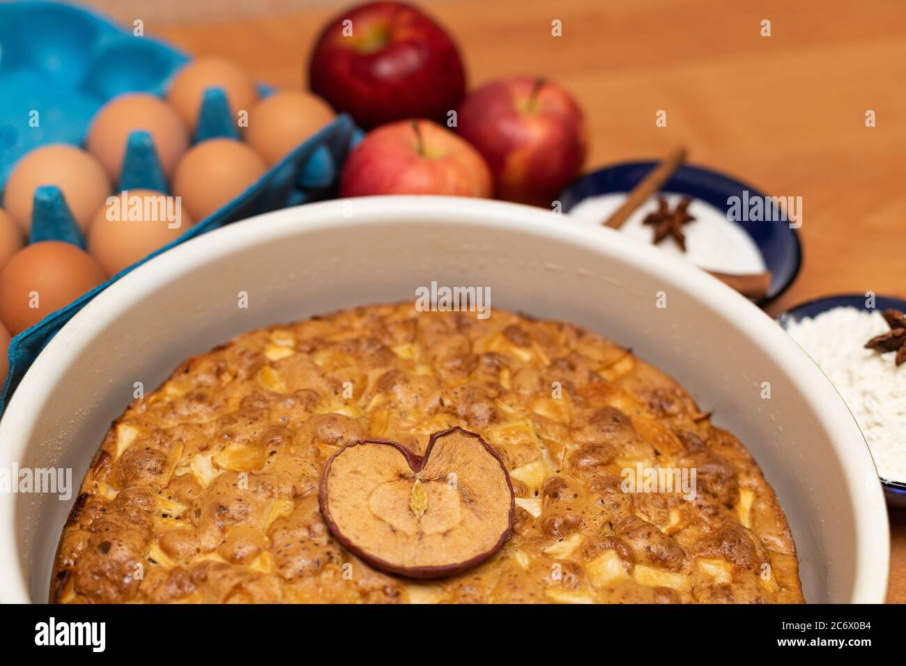 Apfelkuchen mit herzförmigem Apfel auf Holztisch mit Backzutaten Stockfoto