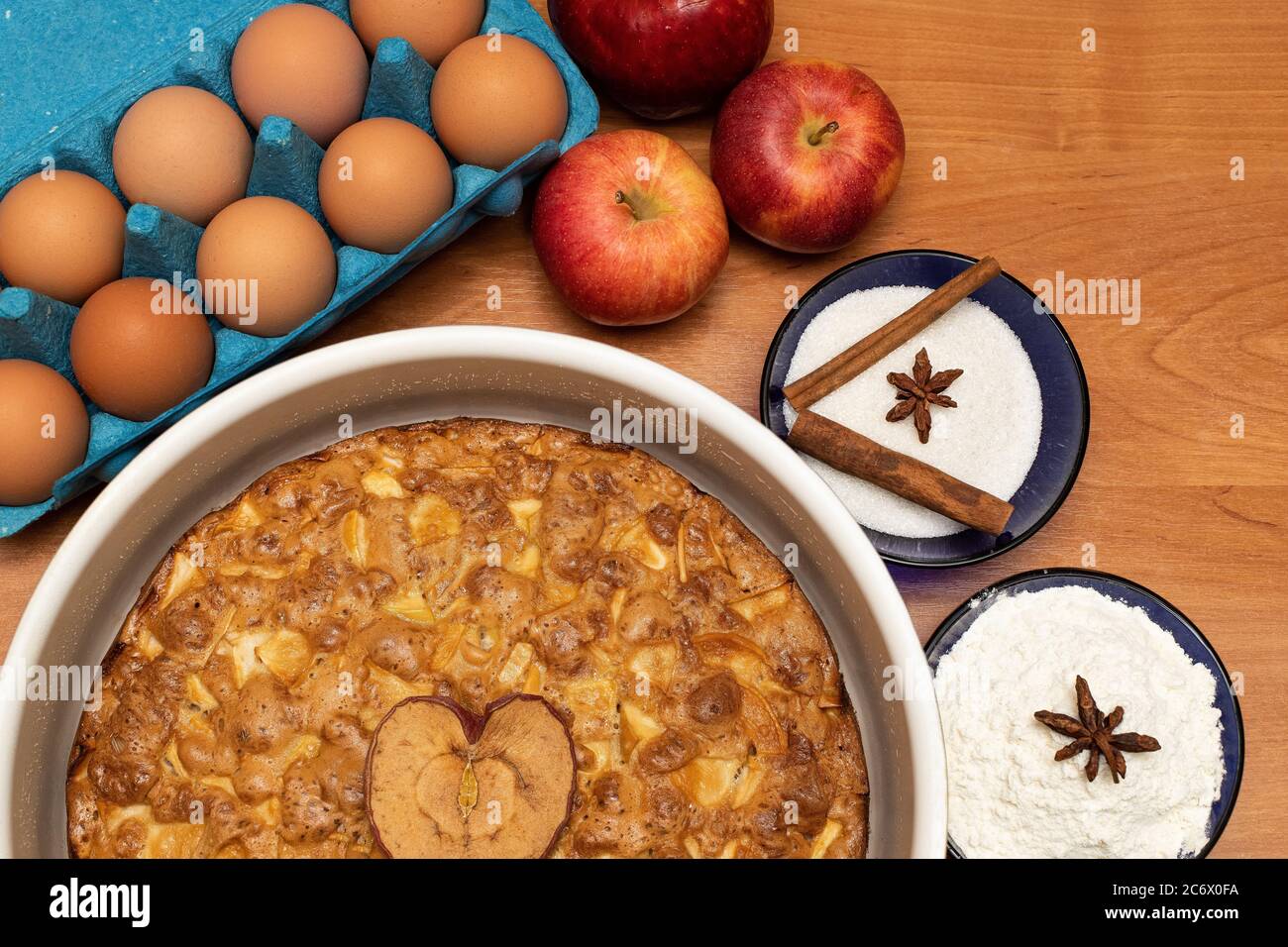 Apfelkuchen auf einem Holztisch mit Backzutaten: Äpfel, Eier, Zucker, Mehl, Zimt und Badian Stockfoto