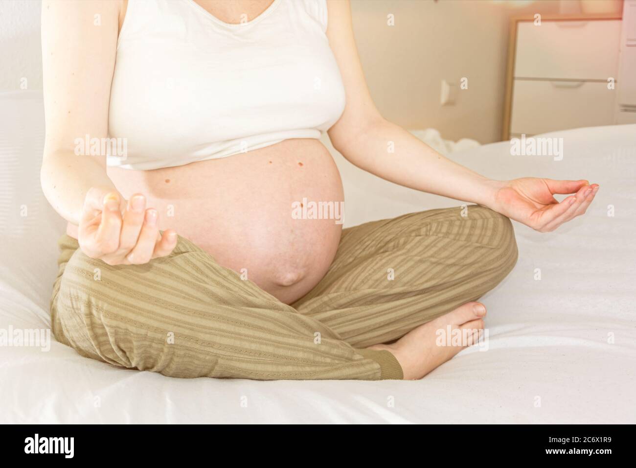 Schwangere Frau meditiert friedlich auf einem Bett Stockfoto
