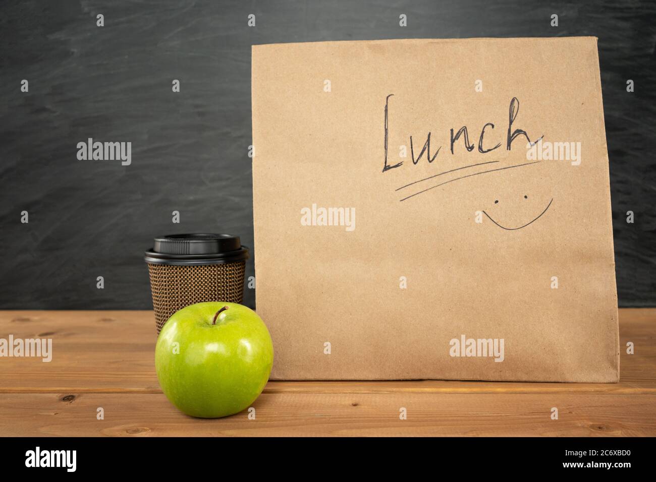 Umweltfreundliche braune Papier-Lunchtasche auf Holztisch mit Apfel und Kaffeetasse. Kreidetafel auf dem Hintergrund. Zurück zur Schule Konzept. Stockfoto