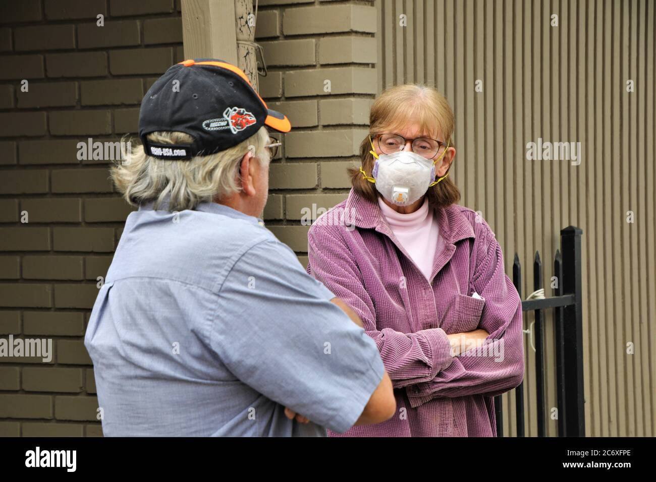 Älterer Mann mit Ballkappe im Gespräch mit unglücklicher älterer Frau Mit Gesichtsmaske während der Pandemie, während sie über die Konstruktion diskutieren Ihr Zuhause Stockfoto