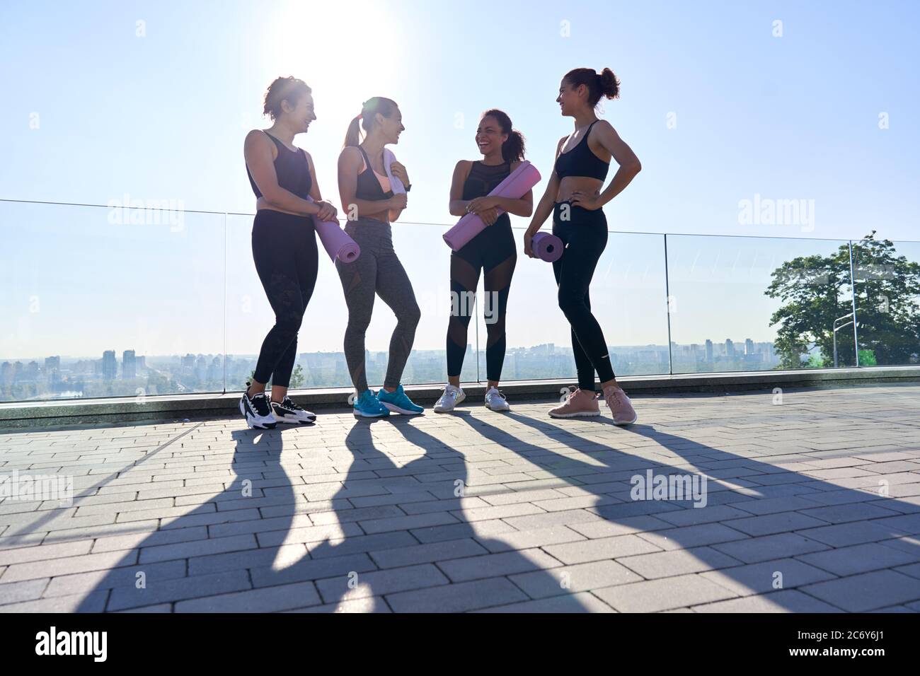 Glücklich vielfältig fit Mädchen Freunde lachen Stand halten Matten Gruppe Yoga-Klasse im Freien. Stockfoto