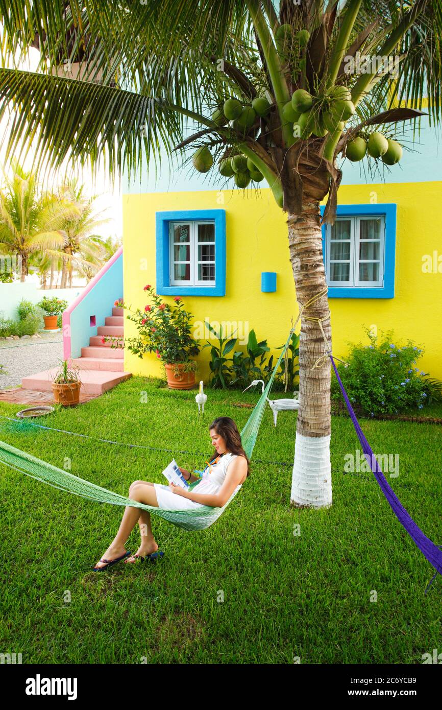 Eine junge Dame liest in einer Hängematte vor einem bunten Bungalow an der Pazifikküste Mexikos. Stockfoto