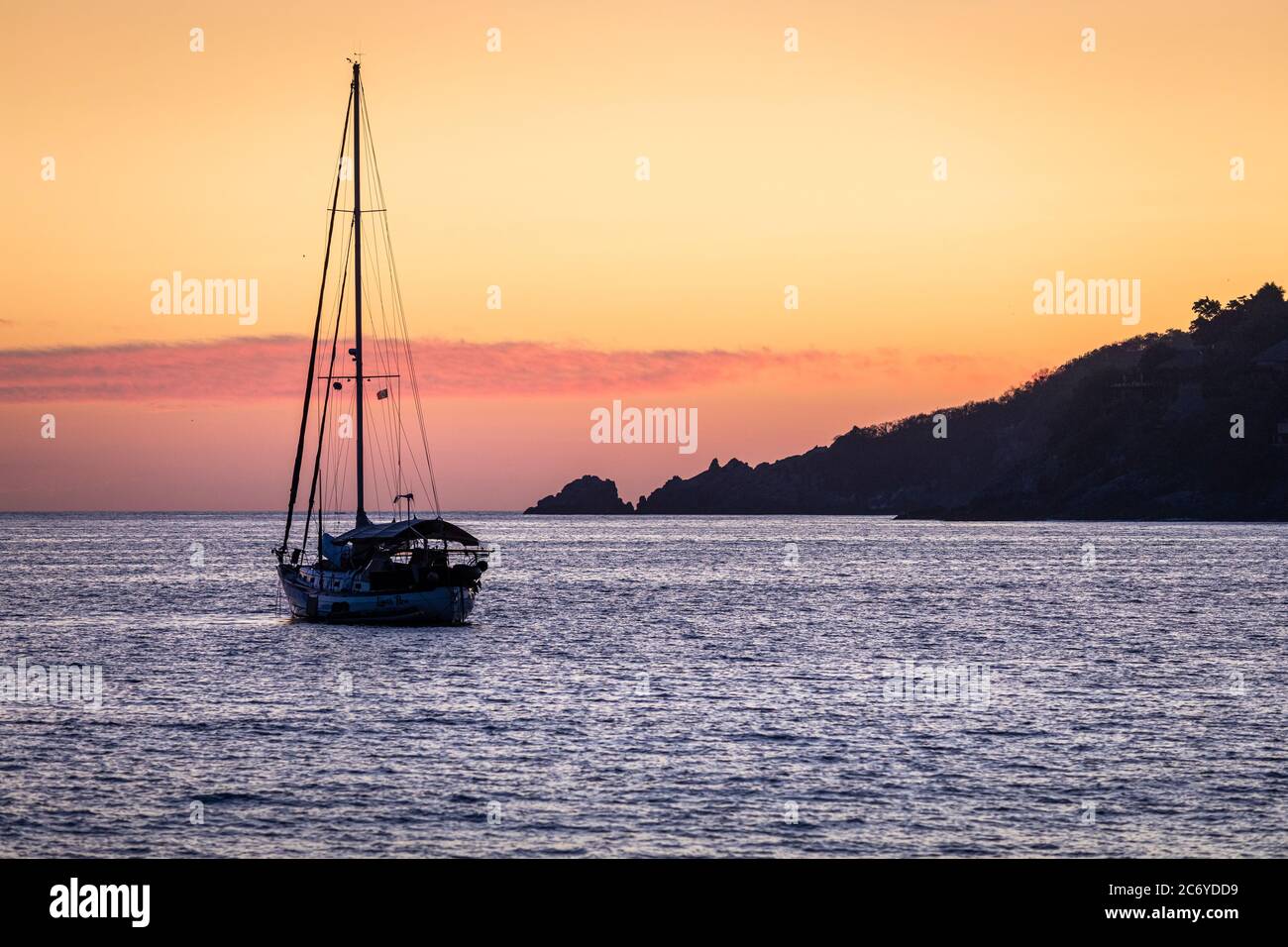 Ein Segelboot schwimmt in der Bucht von Zihuatanejo, Mexiko in der Abenddämmerung. Stockfoto