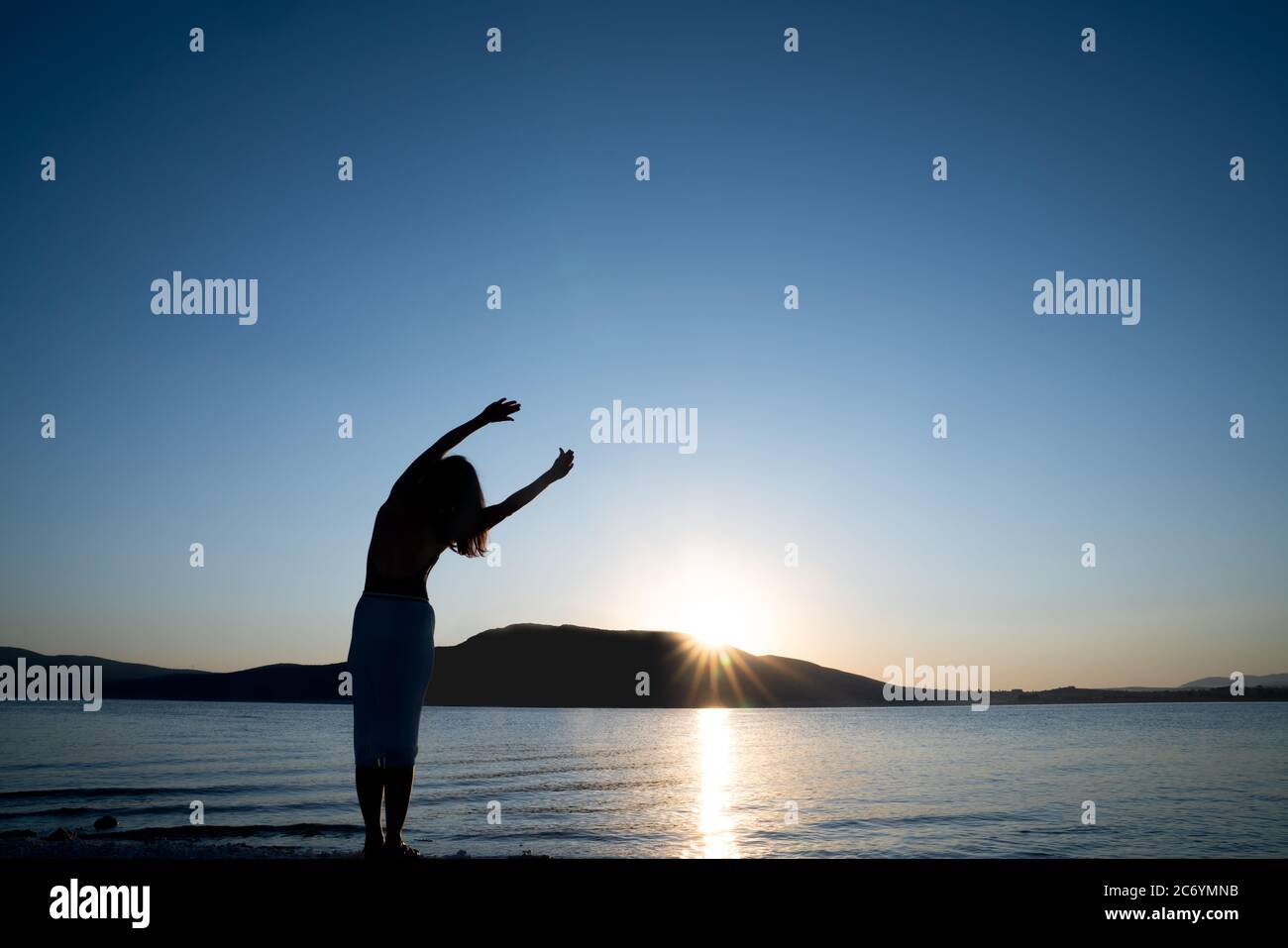 Silhouette der jungen Frau streckt ihren Körper für den Morgensport oder Meditation, gegen die schöne Natur. Gesundheits- und Tourismuskonzept. Stockfoto