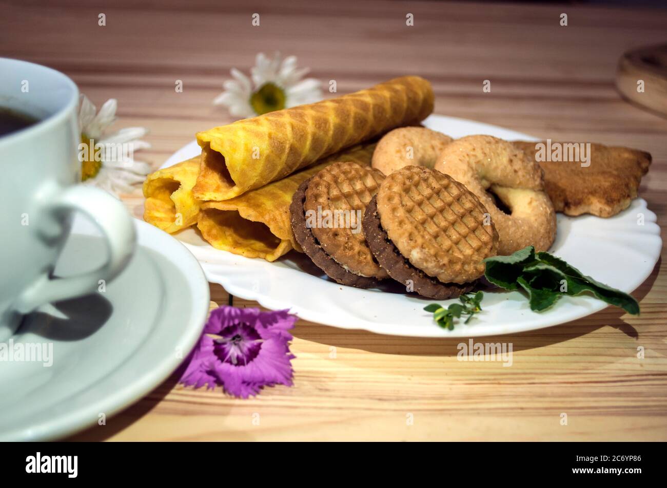 Waffelbrötchen und Kekse auf einem weißen Teller und eine Tasse Kaffee. Waffeln auf der Seite. Komposition auf einem hölzernen Hintergrund. Sichtbare Waffelstruktur, Holz t Stockfoto