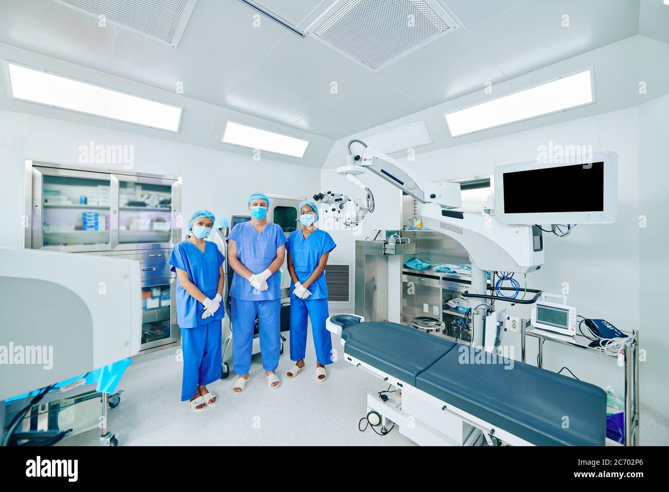 Seriöse medizinische Arbeiter in OP-Uniform, Masken und Handschuhe stehen im OP-Theater Stockfoto