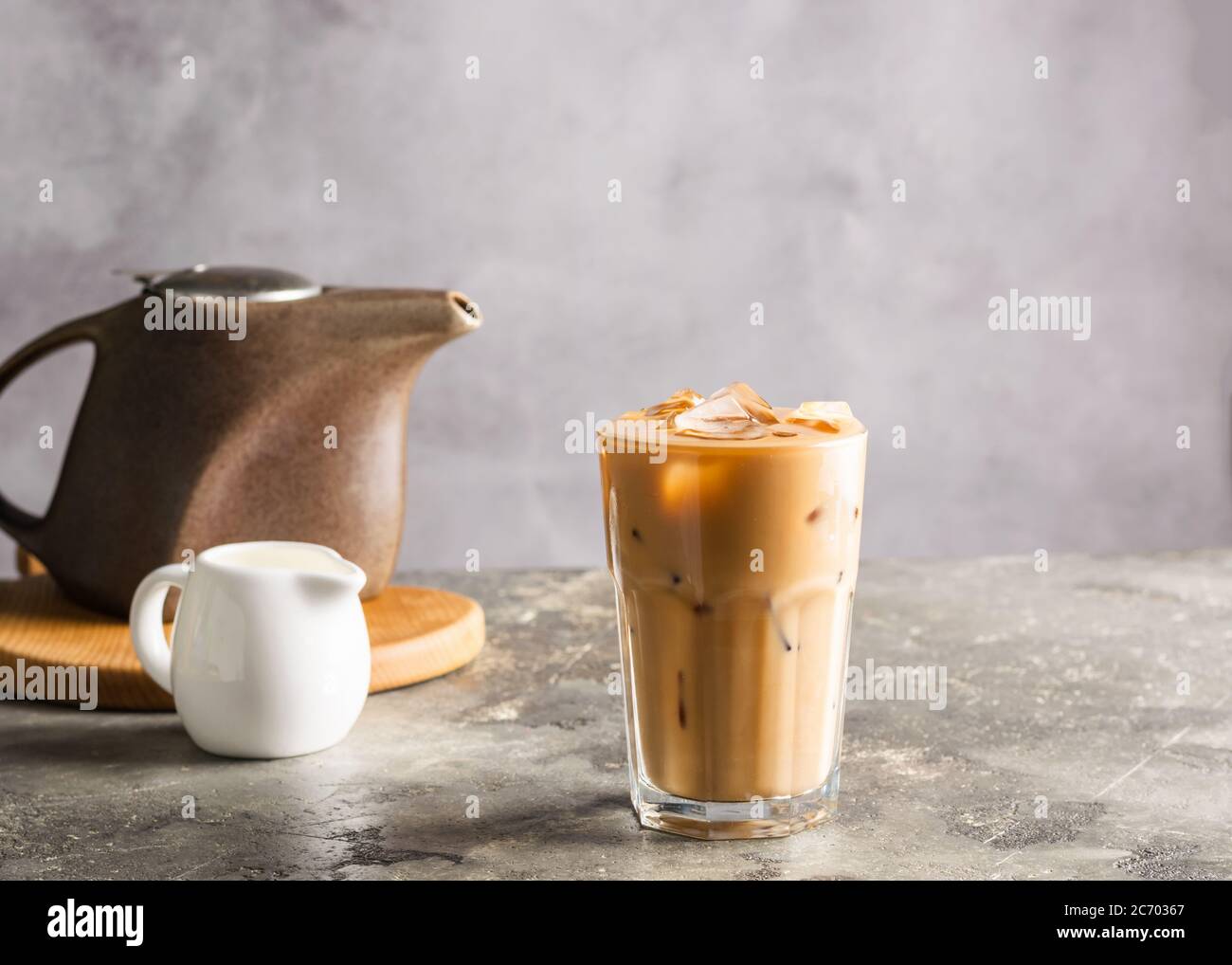 Kalter schwarzer Kaffee mit Eiswürfeln und Milch im hohen Glas. Erfrischendes Kaffeegetränk auf dem grauen Hintergrund des Tisches. Nahaufnahme Stockfoto