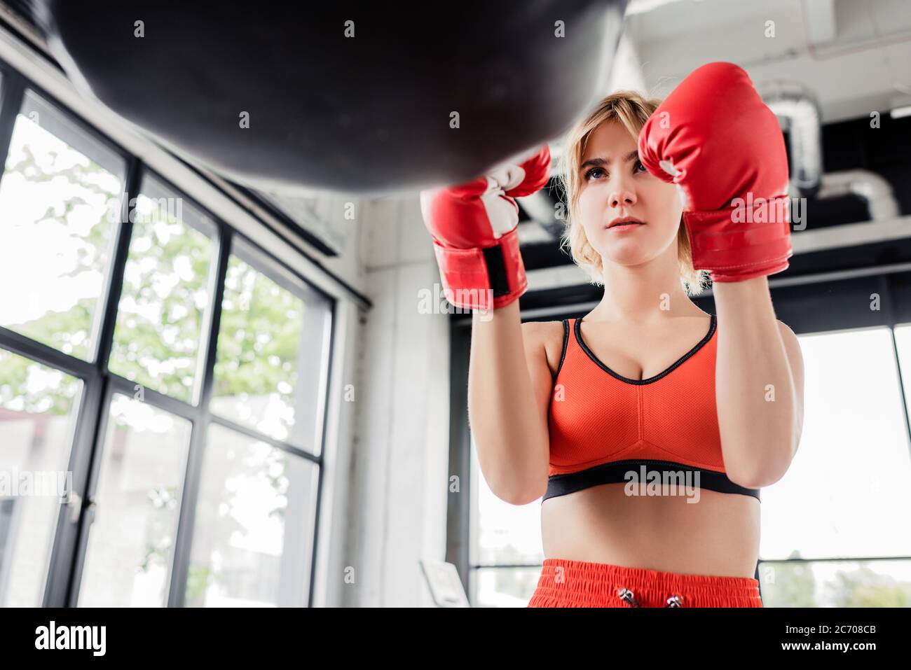 Selektive Fokus der jungen Sportlerin in Boxhandschuhen Blick auf Boxsack Stockfoto