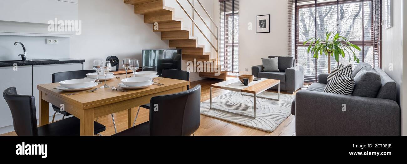 Panorama der stilvollen zweistöckigen Wohnung mit Küche und Essbereich zum Wohnzimmer und Holztreppe zu höheren Etage öffnen Stockfoto