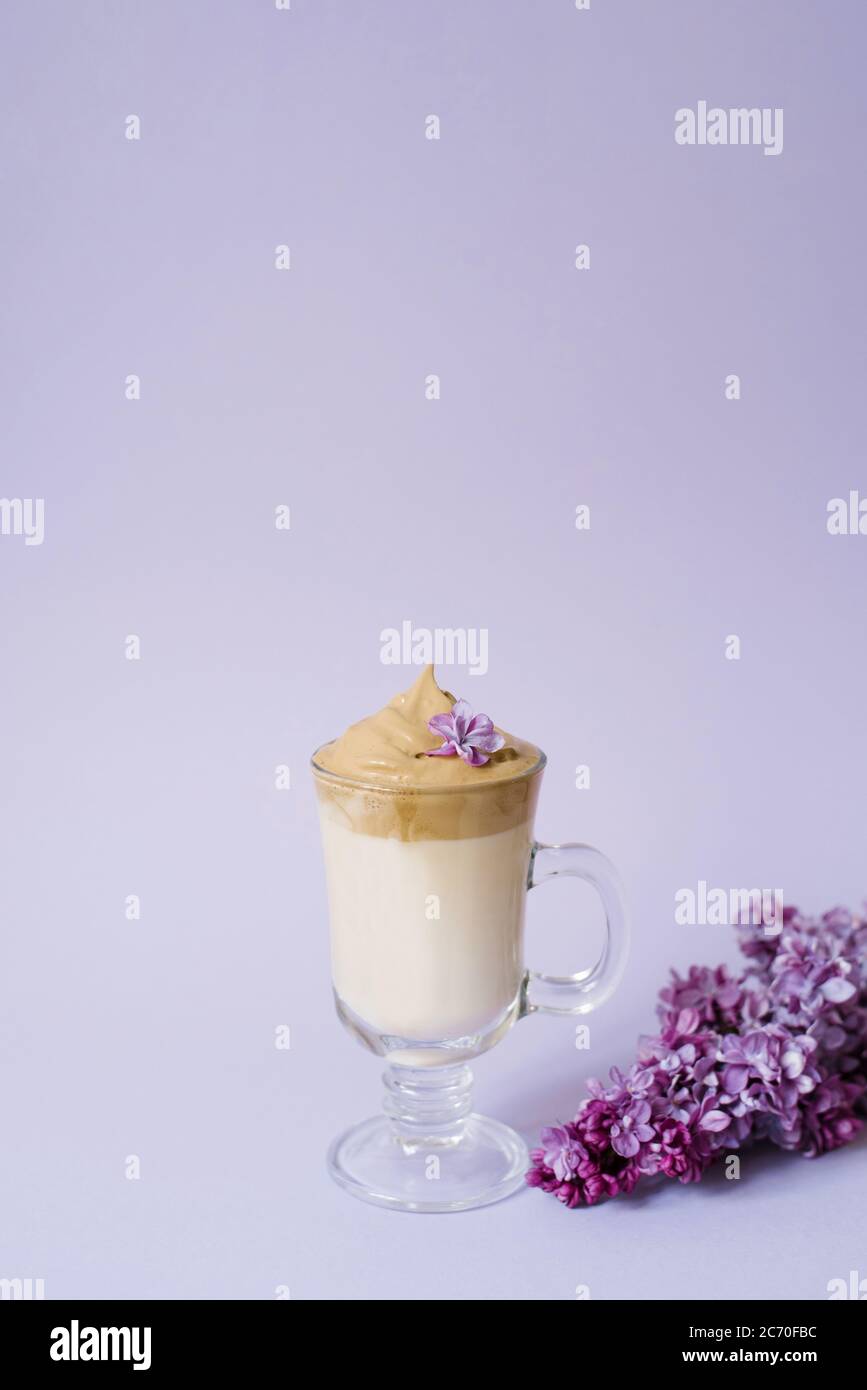 Schöne dalgona trinken einen schaumigen Kaffee in einem transparenten Becher und Blumen lila Il lila Hintergrund. Neben dem Becher ist eine Marshmallow und ein Stockfoto