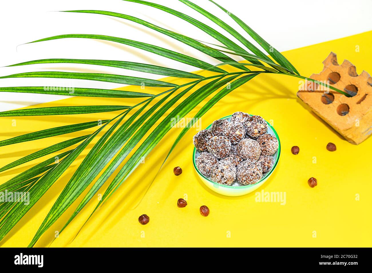 Protein Erdnussbutter Energie Bisse oder Energiebälle. Hausgemachte rohe Schokoladentrüffel mit Nüssen auf Teller mit Palmblatt auf gelbem Hintergrund. Stockfoto