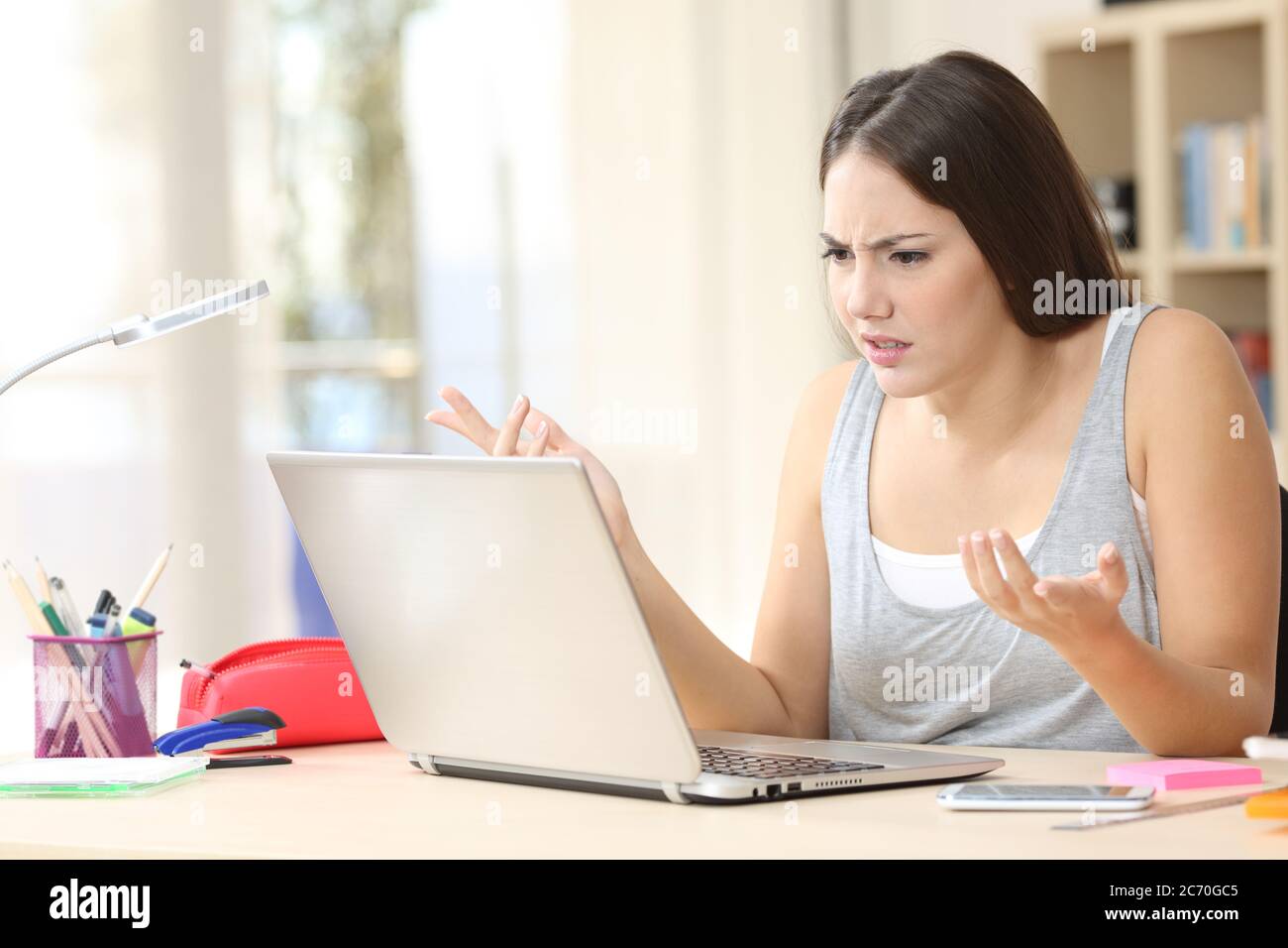 Verärgerte Studentin, die sich ärgerlich über den Laptop auf einem Schreibtisch zu Hause aufpasst Stockfoto