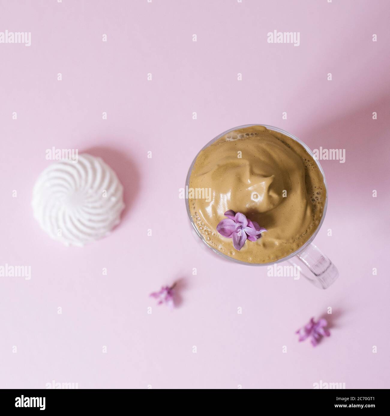 Schöner Dalgon Kaffee trinken. Kaffeebecher mit Schaum und Fliederblüte auf einem lila rosa Hintergrund. Draufsicht Stockfoto