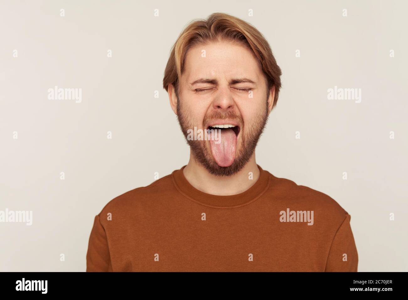 Portrait von lustigen optimistischen Mann mit Bart tragen Sweatshirt Verhalten kindisch frech, zeigt Zunge aus und macht Gesichter, ungehorsam goofy grima Stockfoto