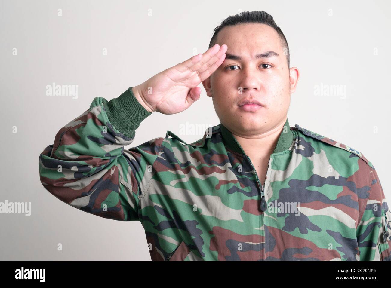 Junge gut aussehende übergewichtige asiatische Mann in militärischen Uniform salutieren Stockfoto