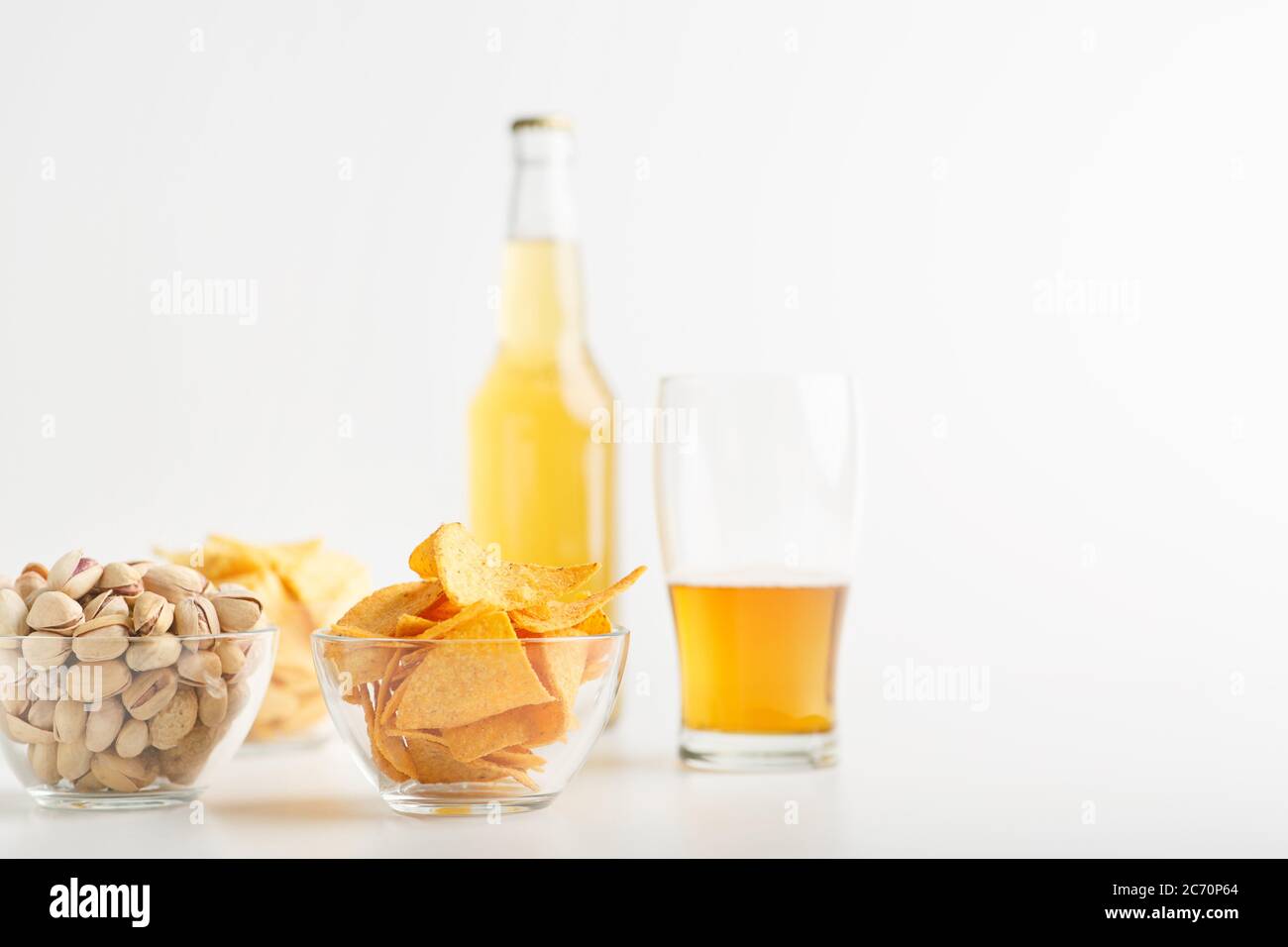 Pistazien, Chips und Nachos in Platten. Glas unvollendetes helles Bier und eine volle Flasche Lagerbier Stockfoto