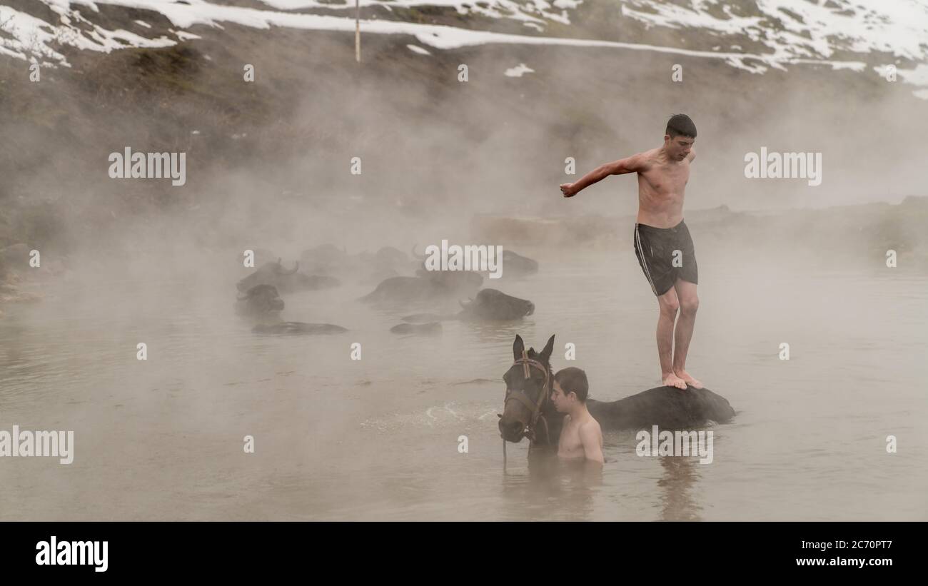 Guroymak, Bitlis, Türkei - Februar 2020: Kleiner Junge springt von seinem Pferd ins Thermalwasser, Tierdusche Stockfoto