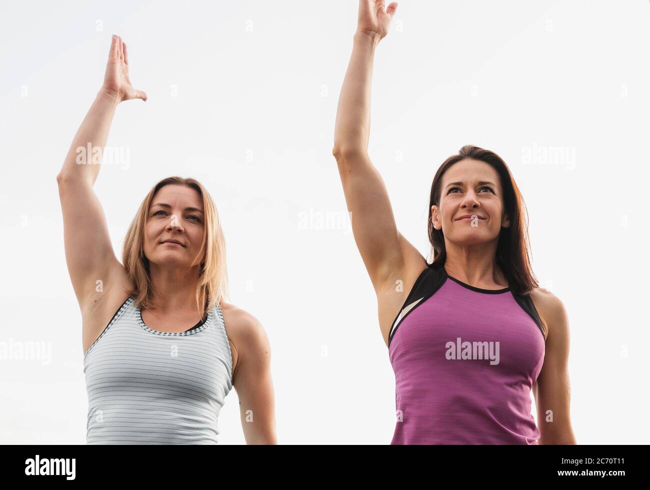 Zwei Frauen trainieren im Freien Stretchübungen, die ihre Arme in der Luft in einem niedrigen Winkel Ansicht in einem gesunden aktiven Lebensstil Konzept heben Stockfoto