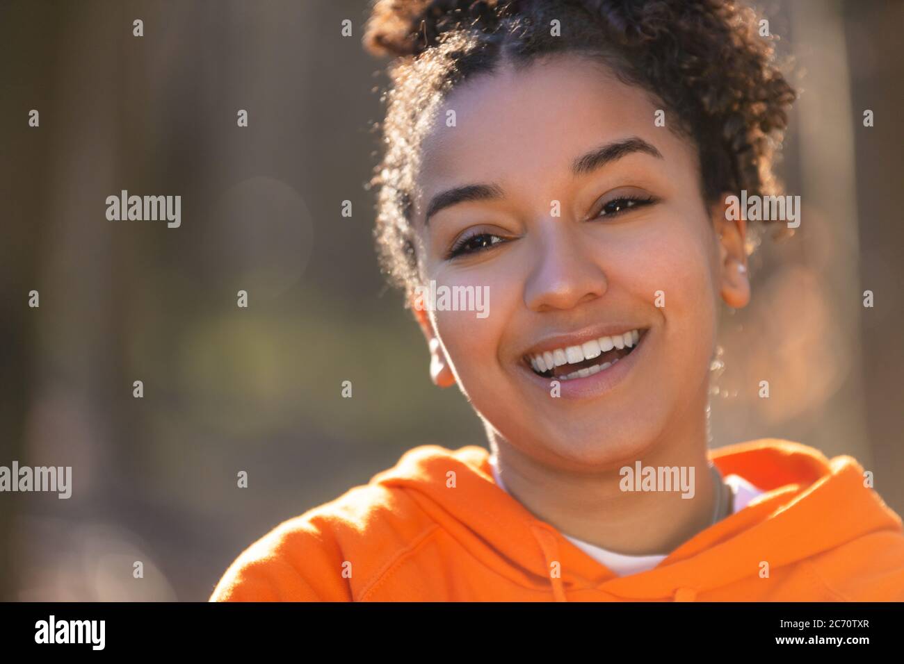 Outdoor-Porträt von schönen glücklich gemischt Rasse biracial afroamerikanischen Mädchen Teenager weibliche junge Frau lächeln mit perfekten Zähnen trägt eine Orange Stockfoto