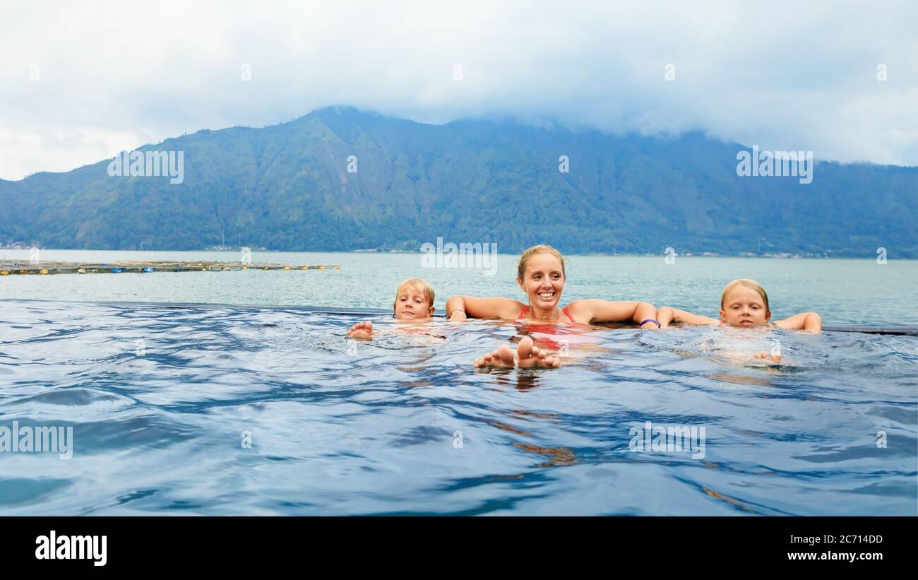 Glückliche Familie im Thermalbad des Vulkans Batur. Reisen Sie in Kintamani, Bali. Mutter, Kinder kühlen im Infinity-Pool mit Blick auf den See. Gesunder Lebensstil Stockfoto