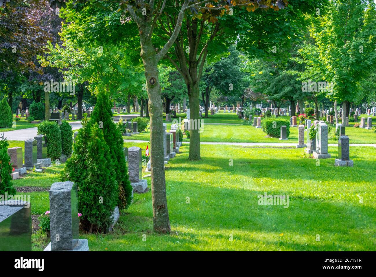 Ein schöner Friedhof mit Grabsteinreihen und gesäumt von Bäumen, Blumen und Spazierwegen, bietet eine friedliche Umgebung für die Familie. Stockfoto