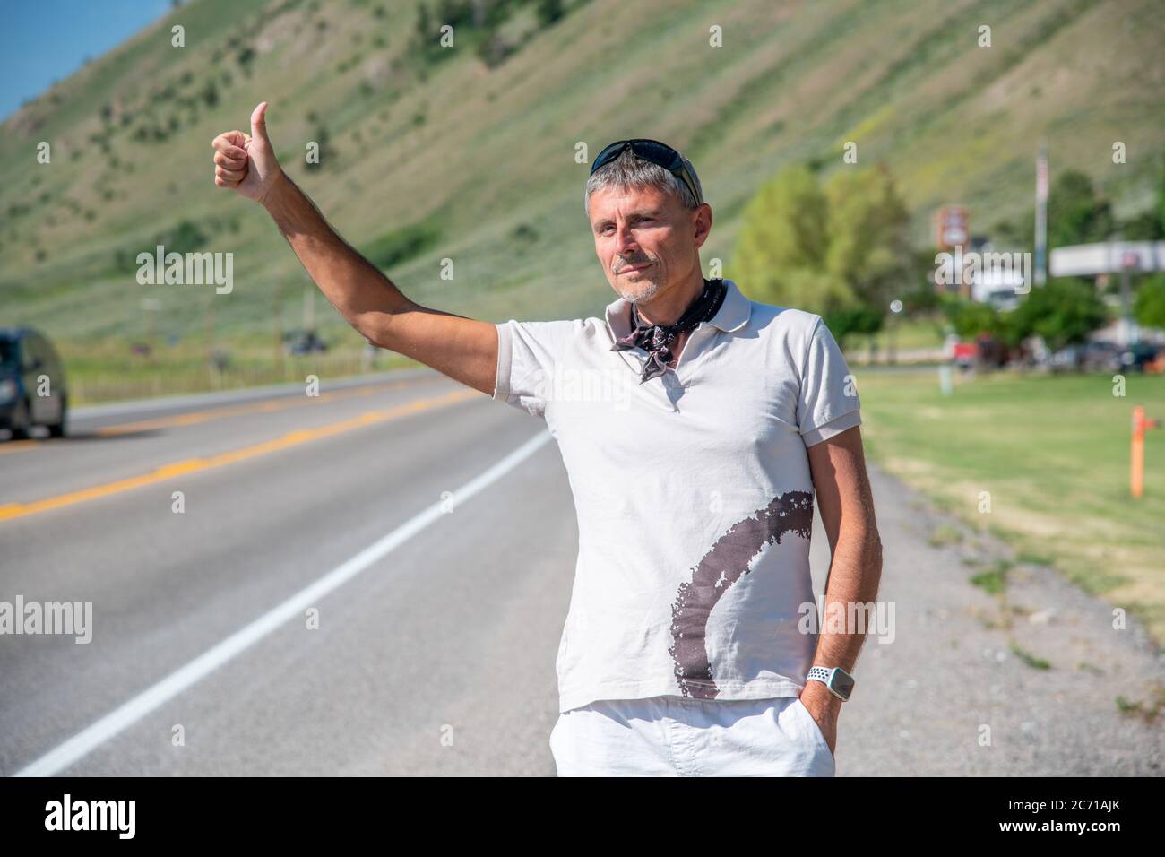 Außenaufnahme eines Reisemannes, der in einem lässigen T-Shirt entlang einer Landstraße trampelt. Reise-, Tourismus- und Urlaubskonzept. Stockfoto