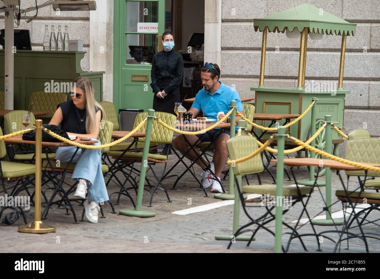 Ein Kellner mit einer schützenden Gesichtsmaske steht beim Essen draußen in Covent Garden, London, nach der Aufhebung weiterer Beschränkungen für Coronavirus-Sperren in England. Stockfoto