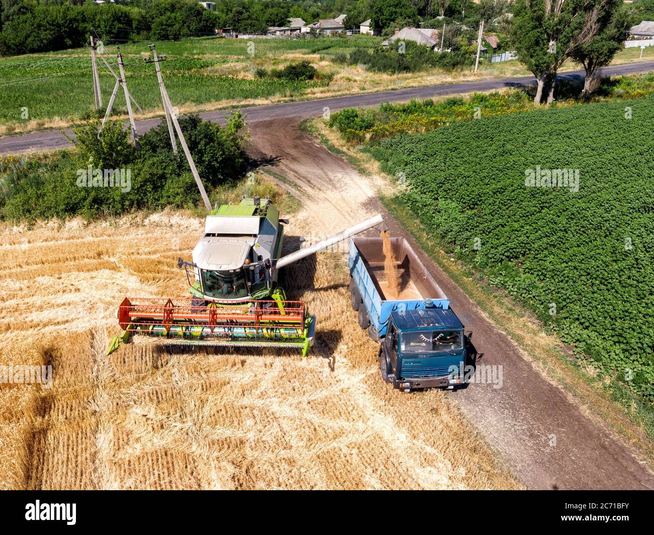 Aerial Drohne Draufsicht große leistungsstarke industrielle Mähdrescher Maschine Entladen bin von Weizen Getreidefeld in LKW auf hellen Sommer oder Tag Stockfoto
