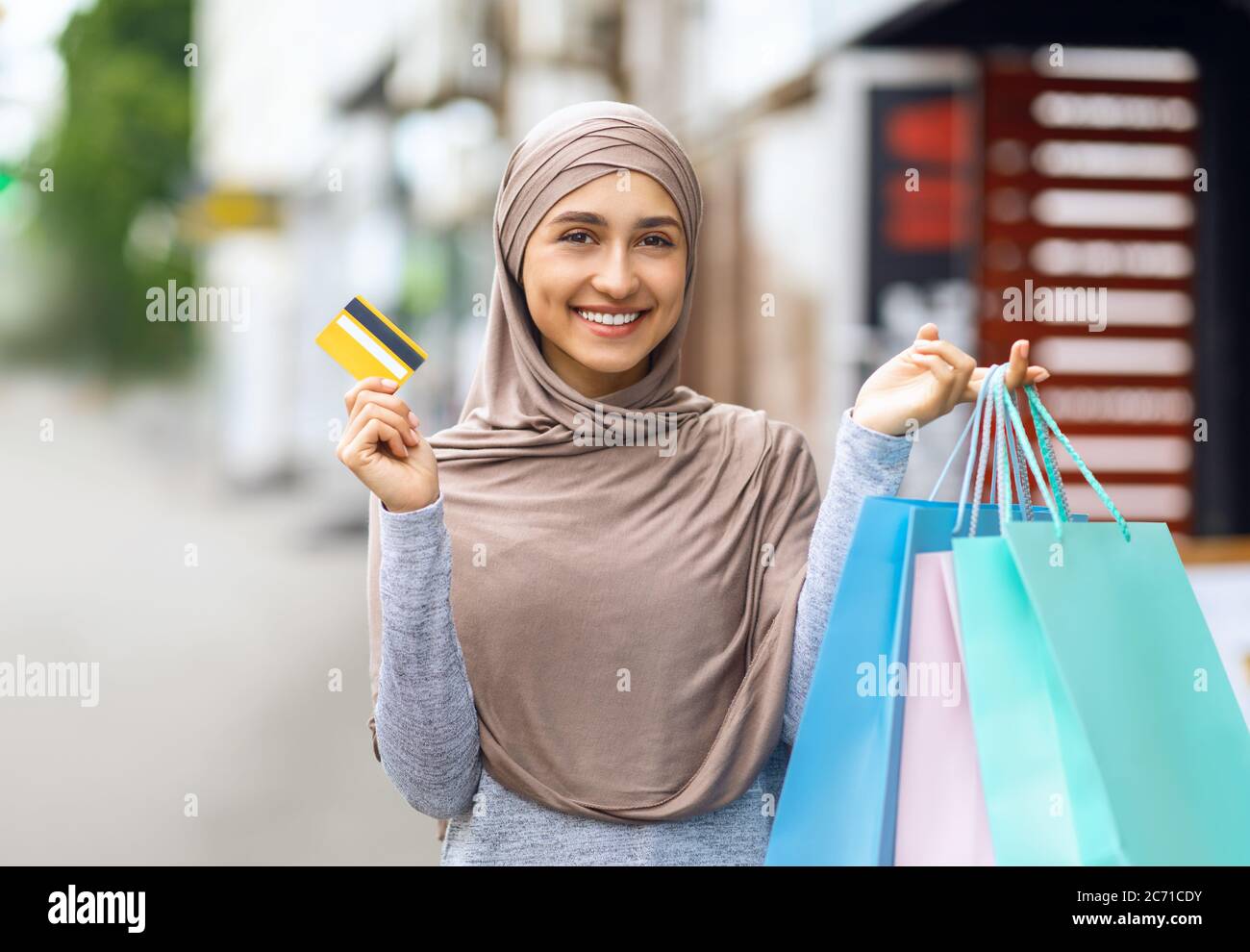 Positive arabische Frau mit Einkaufstaschen und Kreditkarte Stockfoto