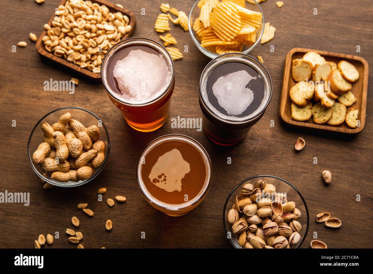 Dunkles, helles, ungefiltertes Bier in Gläsern und knusprige Vorspeisen auf Tellern auf Holztisch Stockfoto