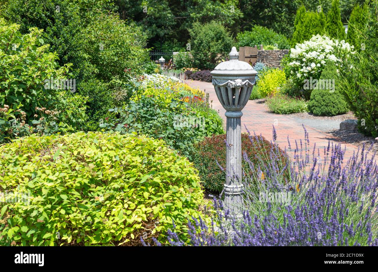 Landschaft mit formalem Garten mit bunten Sträuchern und blühenden Pflanzen mit Urne an hellen sonnigen Tag Stockfoto