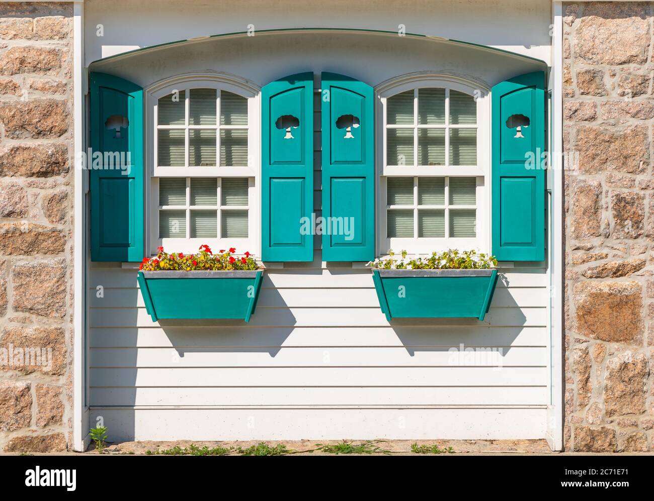 Teilweise Front außen von weißen Hütte mit blauem Fensterläden und Fensterboxen mit roten und weißen Impatiens Blumen Stockfoto