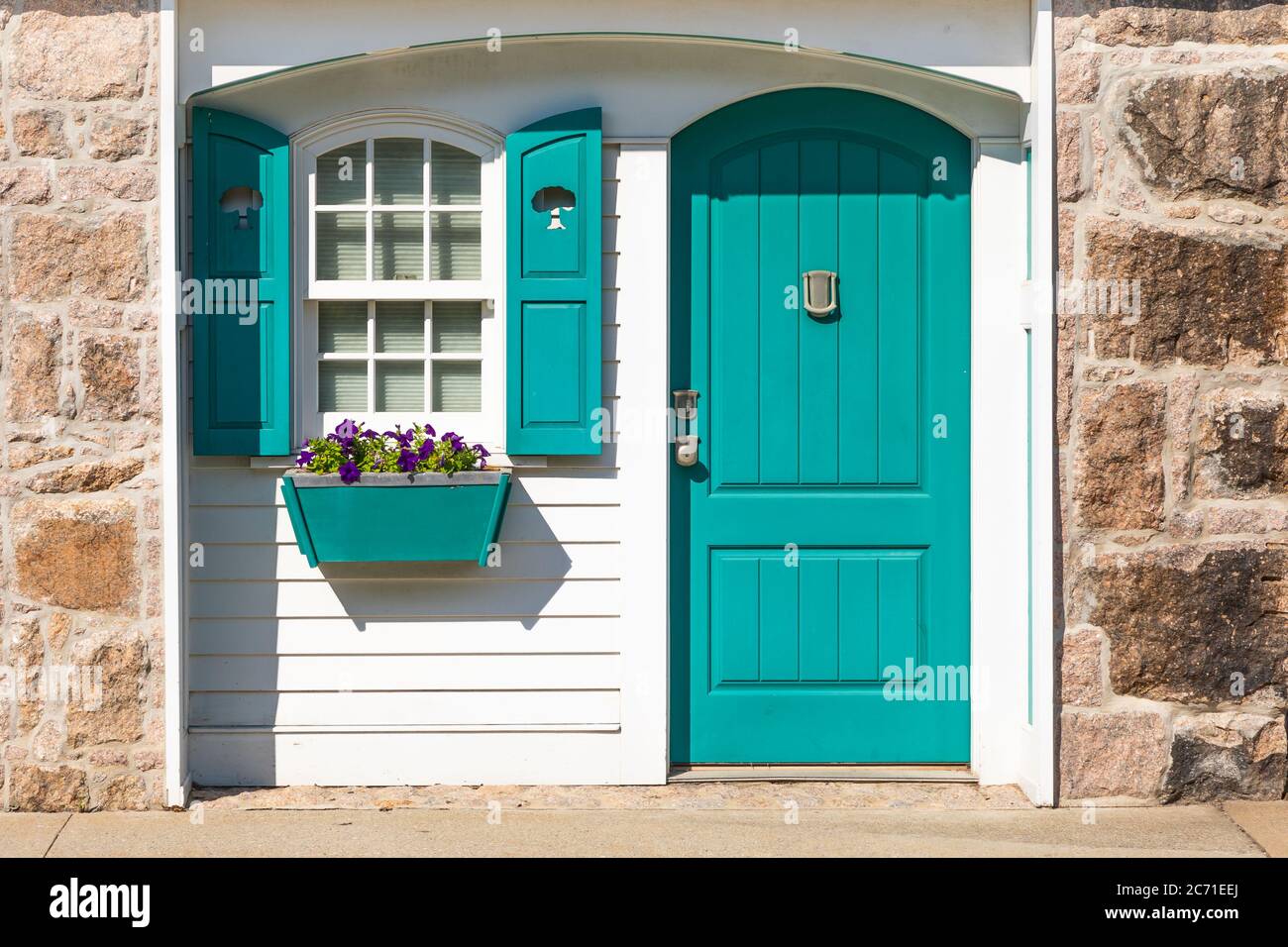 Teilweise Front außen von weißen Hütte mit blauem Fensterläden und Tür und blaugrün Fensterbox mit lila Petunien an hellen sonnigen Tag Stockfoto