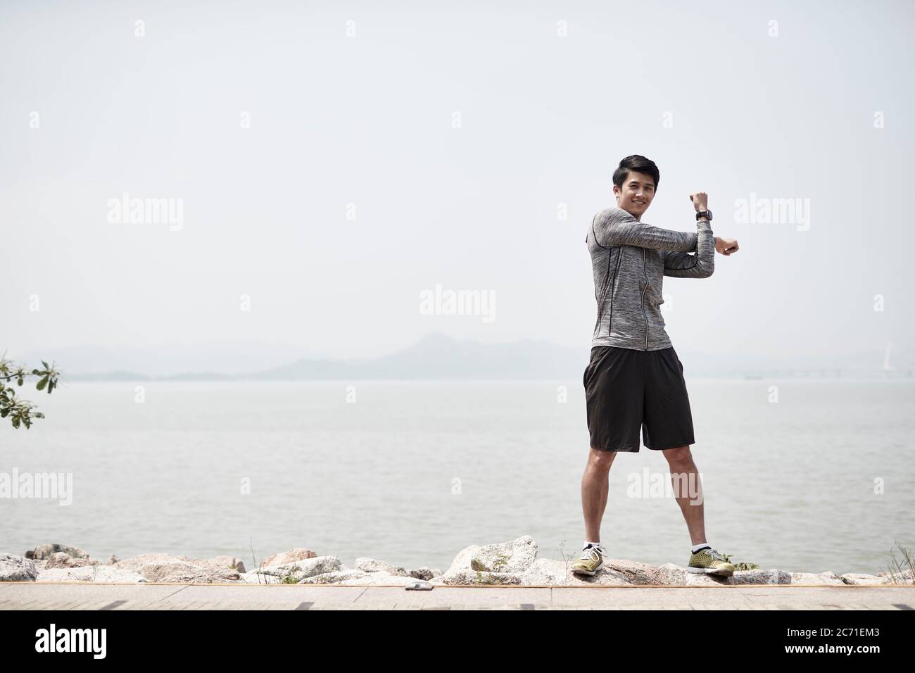 Junger asiatischer Erwachsener, der die Arme im Freien am Meer ausdehnt Stockfoto