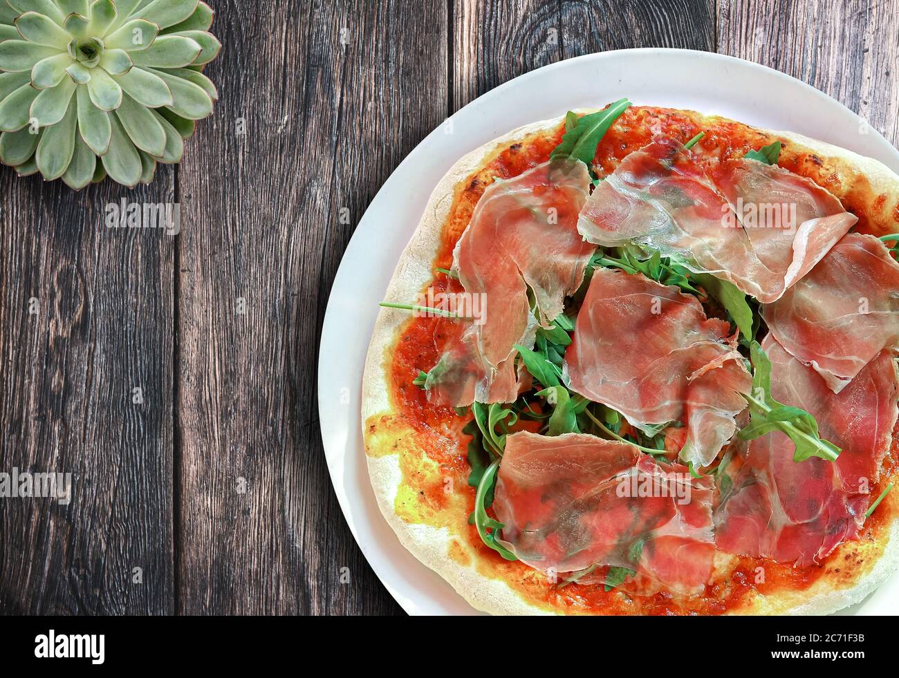 Blick von oben auf frische hausgemachte leckere italienische Pizza mit Serrano Schinken und Rucola auf rustikalem Holztisch Stockfoto