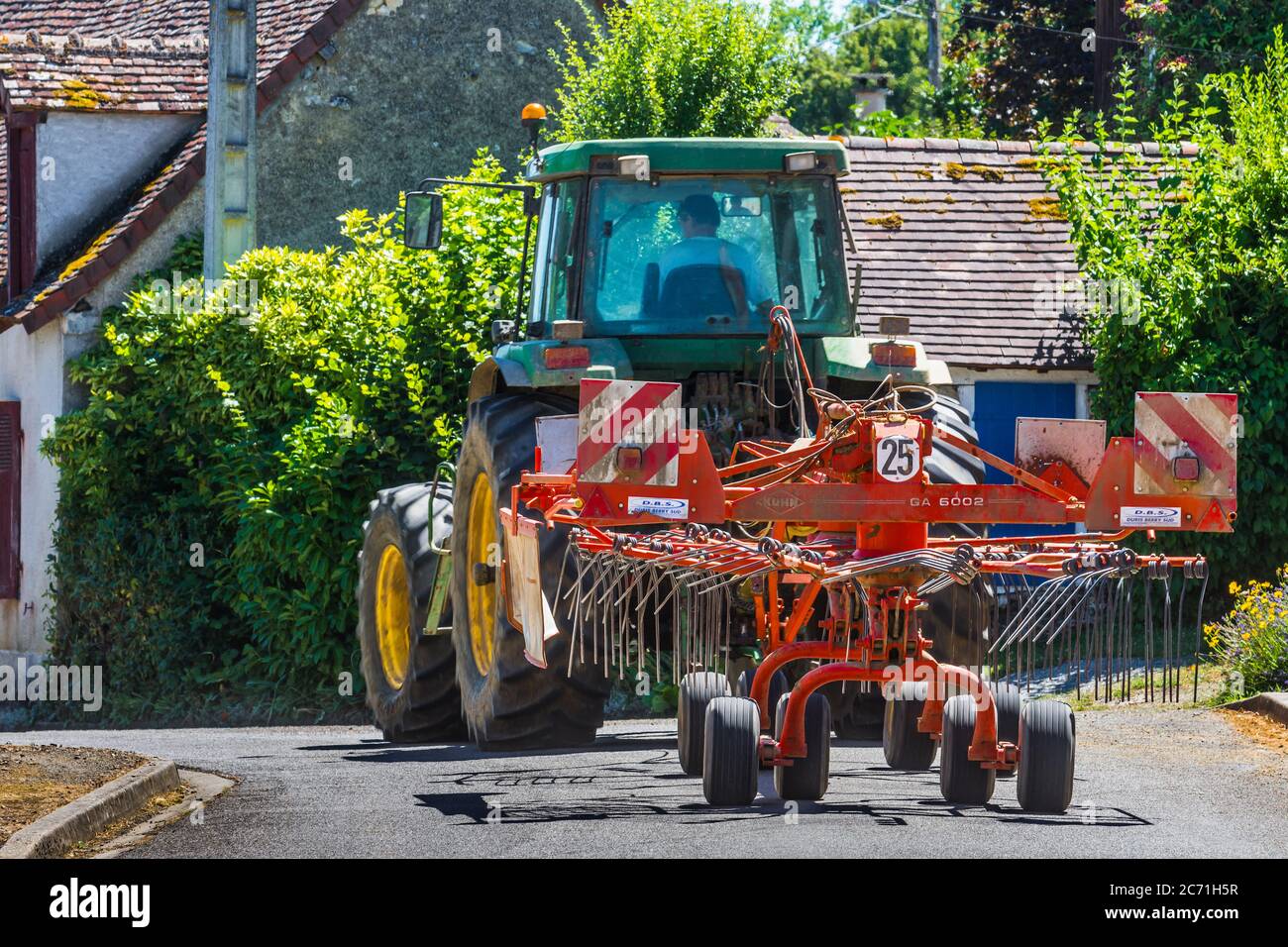 John Deere 7800 Traktor und Kuhn GA5002 Heuwender verhandeln gewundenen ländlichen Dorfstraße - Indre, Frankreich. Stockfoto