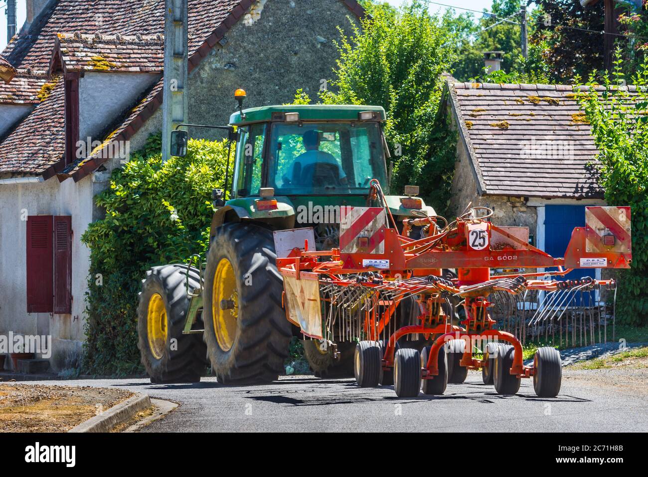 John Deere 7800 Traktor und Kuhn GA5002 Heuwender verhandeln gewundenen ländlichen Dorfstraße - Indre, Frankreich. Stockfoto