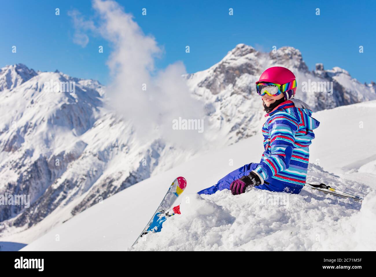 Happy junge Mädchen in hellen Sport-Outfit sitzen auf dem Schneehaufen in den Berg über hohe Gipfel Blick zurück zur Kamera Stockfoto