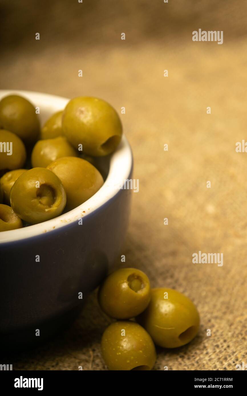 Grüne Oliven in einer Keramikschale auf einem Hintergrund aus grobstrukturiertem Sackleinen. Nahaufnahme Stockfoto