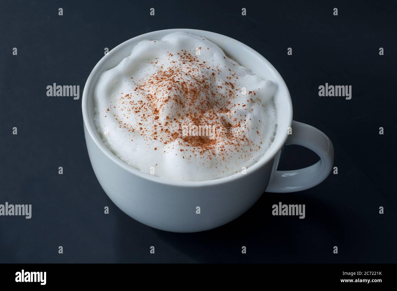 Kaffee Latte mit Milchschaum und Zimt bestreut in einer großen weißen Tasse auf einem dunklen Hintergrund. Dieses heiße Getränk ist perfekt für den Morgen und wenn Sie es brauchen Stockfoto