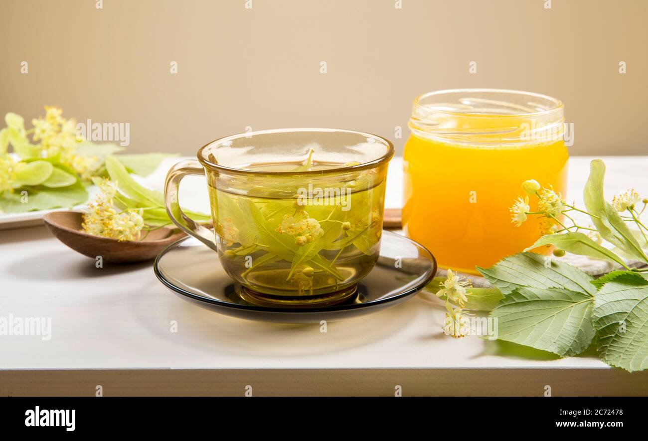 Tilia platyphyllos bekannt als großblättrige Linden Kräutertee mit frisch gepflückten Blüten und Glas Honig mit Baumblättern und Ästen mit Blüten. Stockfoto