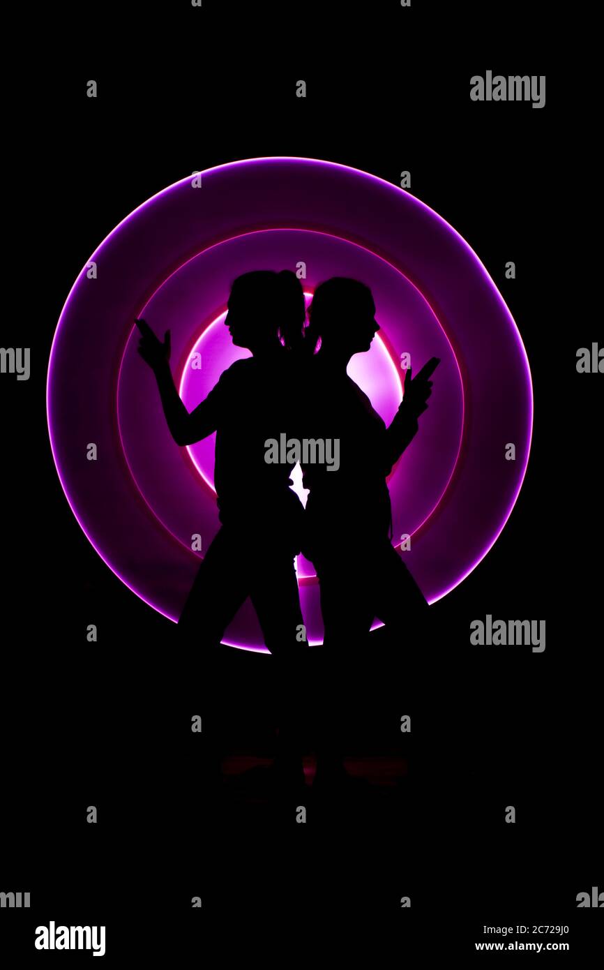 Profil Silhouette von zwei Frauen tun als drei lustige Damen mit Pistolenförmigen Fingern. Abstrakte Kreisform mit hellem Säbel im Hintergrund. Stockfoto