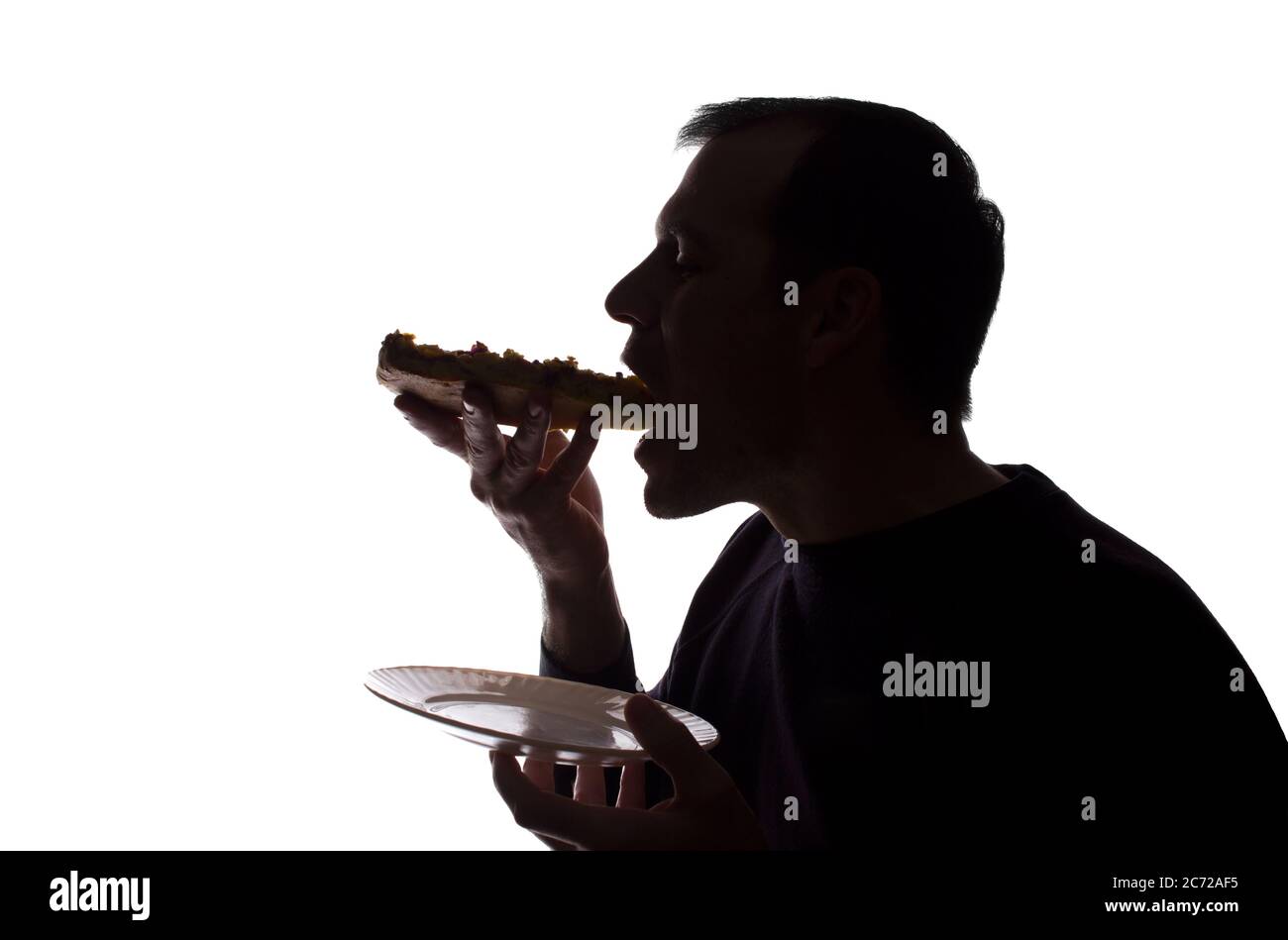 Porträt eines jungen Mannes essen eine Pizza in der Hand, unrasiert, Seitenansicht - dunkel isoliert Silhouette Stockfoto