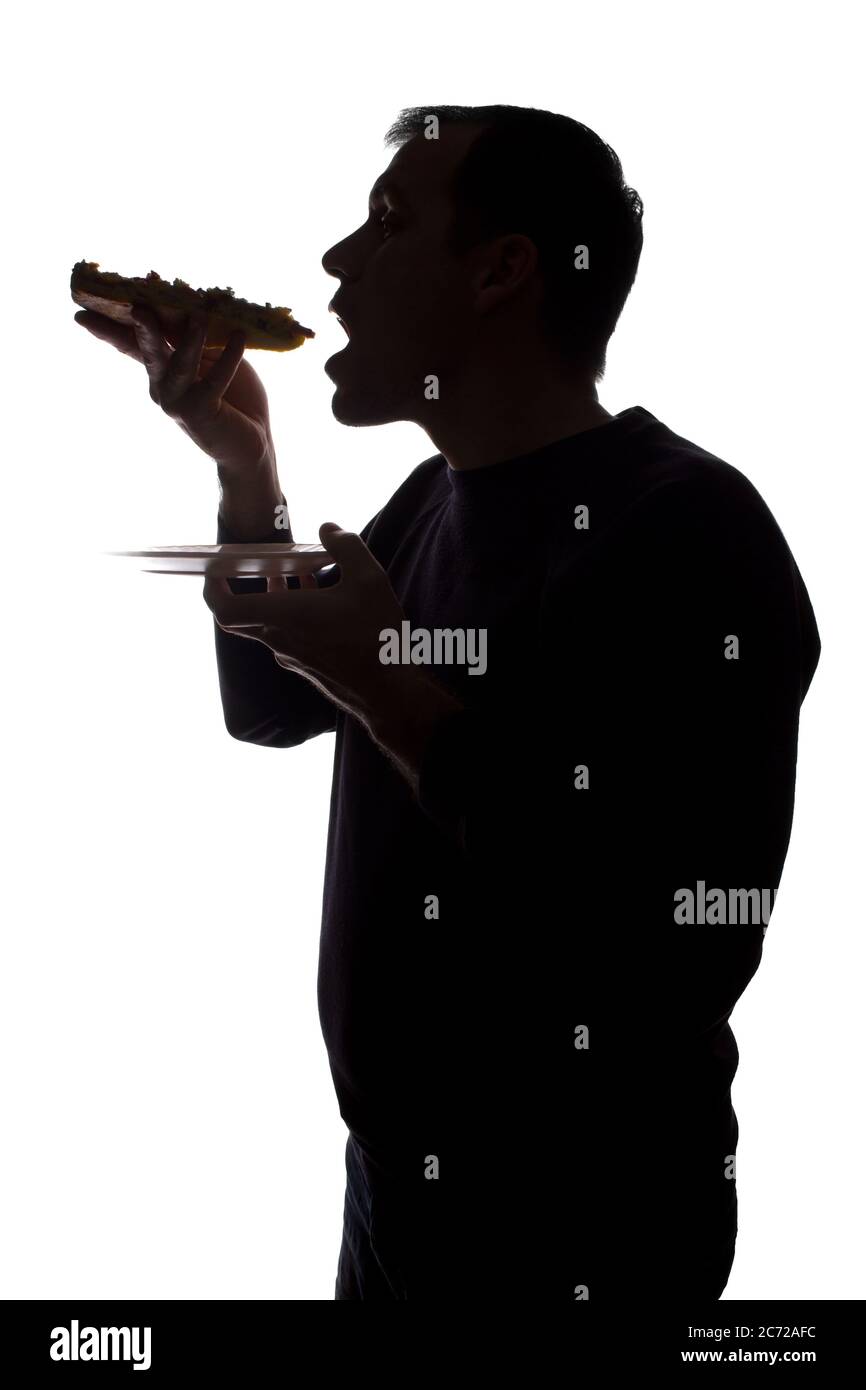 Porträt eines jungen Mannes essen eine Pizza in der Hand, unrasiert, Seitenansicht - dunkel isoliert Silhouette Stockfoto