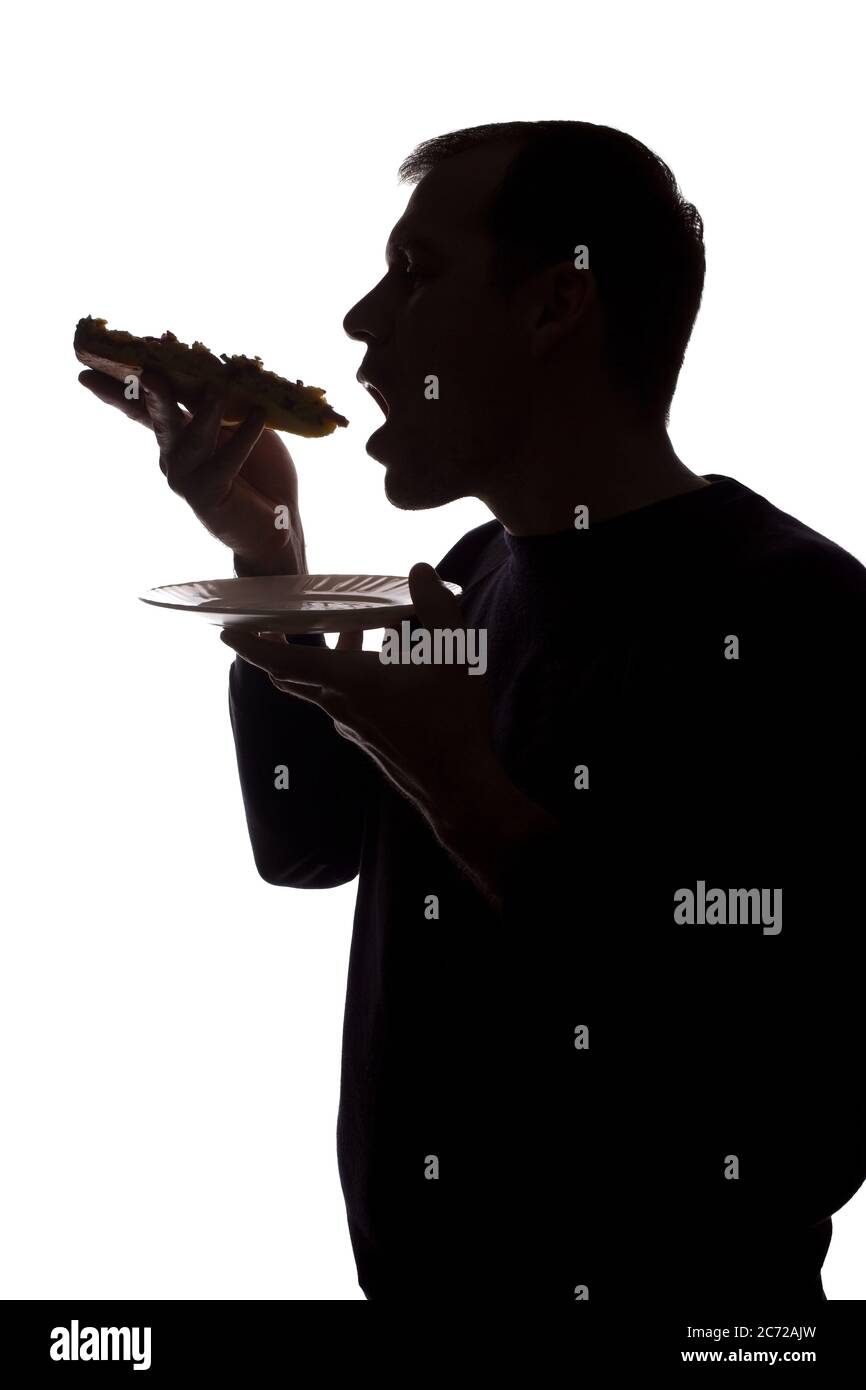 Porträt eines jungen Mannes essen eine Pizza in der Hand, unrasiert, Seitenansicht - dunkel isoliert Silhouette Stockfoto