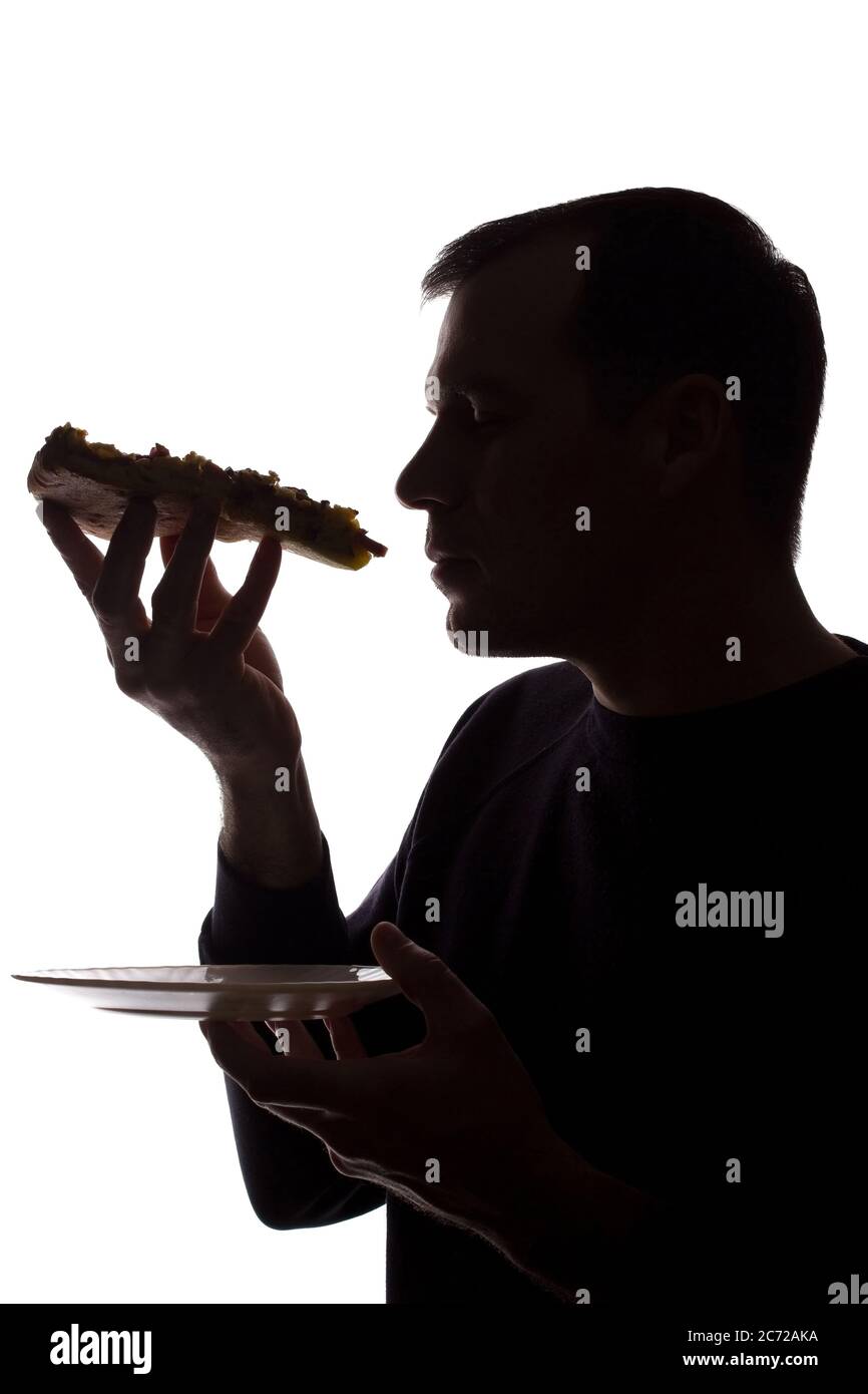 Porträt eines jungen Mannes essen eine Pizza in der Hand, unrasiert, Seitenansicht - dunkel isoliert Silhouette Stockfoto