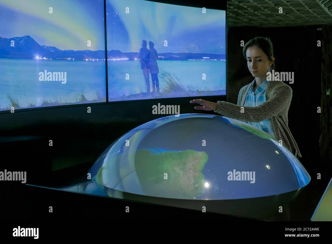 MOSKAU, RUSSLAND - 05. JUNI 2019: Smart Expo. Frau mit interaktivem Modell der Erde in dunklen Raum des Multimedia-Museum, Ausstellung mit wenig Licht Stockfoto