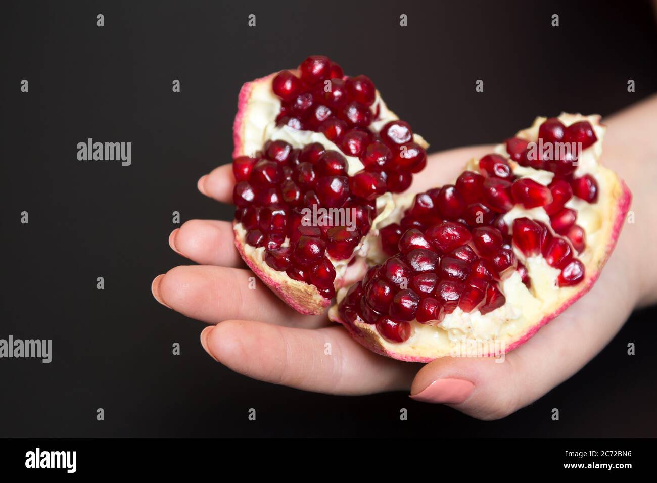 Gereinigte Granatapfel-Frucht in einer weiblichen Hand auf schwarzem Hintergrund Stockfoto