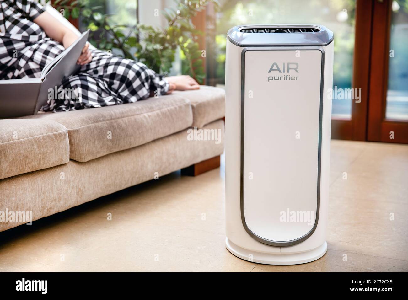 Luftreiniger reinigt die Luft. Moderner Luftreiniger reinigt die Luft im Wohnzimmer mit Frau auf der Couch liegen. Logo auf dem Gerät wurde in erstellt Stockfoto